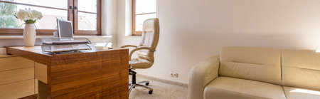 Warm home office with wooden desk, beige leather sofa and chairの写真素材