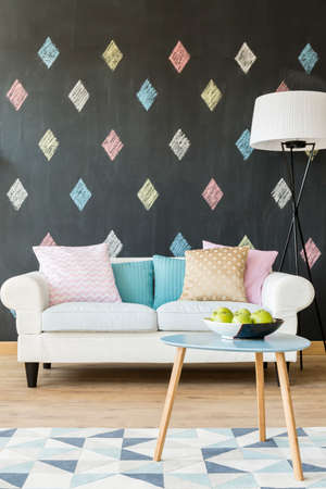 Image of a new style interior with white sofa, pastel cushions, small table, lamp and blackboard wallの写真素材