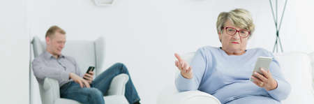 Shot of an older woman sitting worried with mobile phone in her hand with the man sitting laid-back...