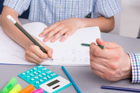 Close up of a small boy studying math with a private teacher, doing notes in his notebook