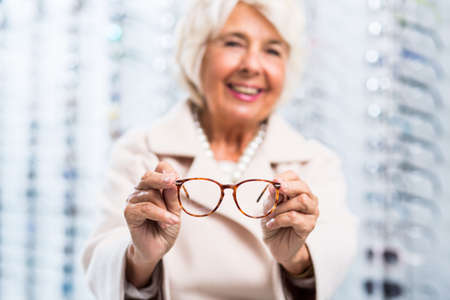 Photo of a smiling elderly woman in the blurred background showing silcrete glasses to the camera