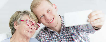 Close shot of elder woman with red glasses and young man taking them a selfie