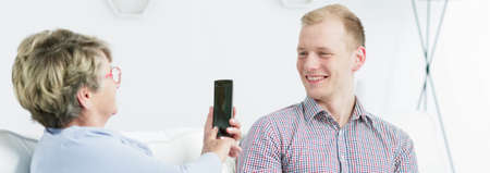 Close shot of elder woman taking mobile photo of a young manの写真素材