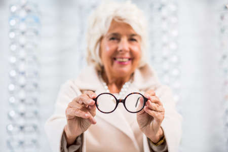 Elderly woman in the blurred background presenting round, trendy glasses to the cameraの写真素材