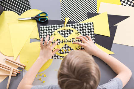 Close-up of young boy doing a picture from black and white paper and yellow cut out on itの写真素材