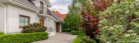 Panoramic photo of an elegant detached house with cobbled front yard and a vast well-groomed gardenの写真素材