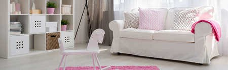Light child room with white regale, sofa, rocking horse and pink carpet