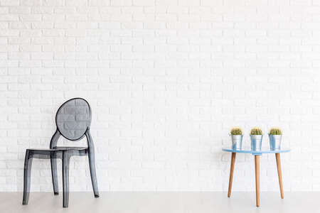 Shot of a transparent chair and a table with three cactuses in a room with a white brick wallの写真素材