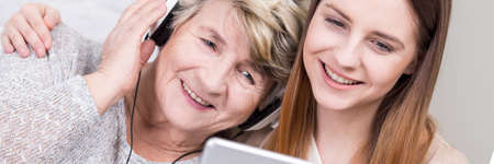 Older grandmother listening her young granddaughter's music on headphones from tabletの写真素材