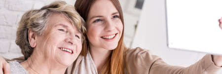 Young granddaughter teaching smiling grandmother how to do selfie with tabletの写真素材