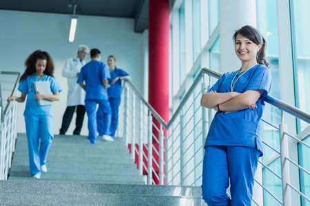 Happy young doctor rests on the railing of the stairs where there are also other interns and supervising them  doctorの写真素材