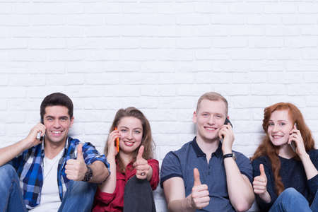 Shot of a group of friends talking on their phones and showing thumbs upの写真素材