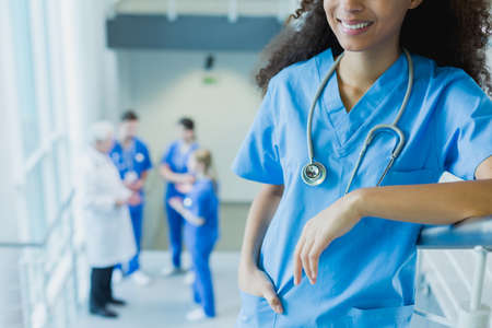 Smiling female intern rests on the railing and her colleagues talking in the backgroundの写真素材