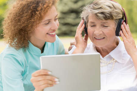 Shot of a young nurse showing something on the screen to retired woman wearing headphones