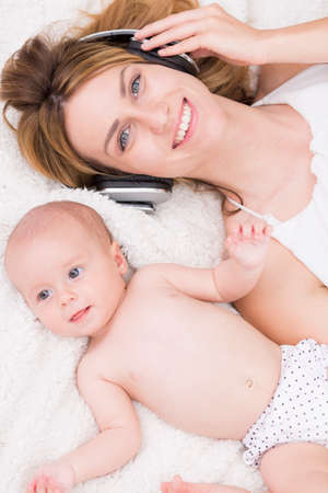 Shot of a smiling mother wearing headphones, lying on the bed with her small daughterの写真素材