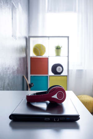 Closeup of red headphones lying on a laptop with colorful shelf in the backgroundの写真素材