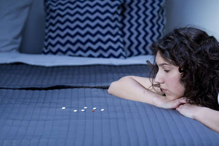 Difficult decision- dangerous pills on bed and young womanの写真素材