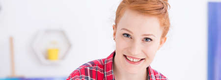 Portrait of a young ginger woman smiling, posing on a light background