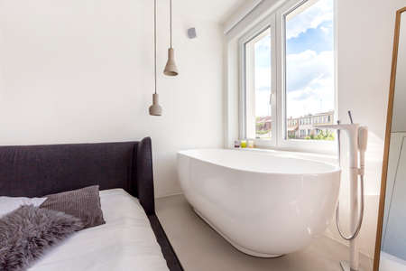 Cropped shot of a spacious bathtub standing by a window in bedroomの写真素材