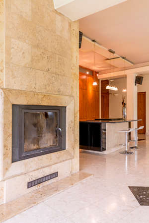 Stone fireplace in a vast house interior, with kitchen island in the backgroundの写真素材