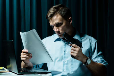 Shot of a focused man holding a gun and reading some files