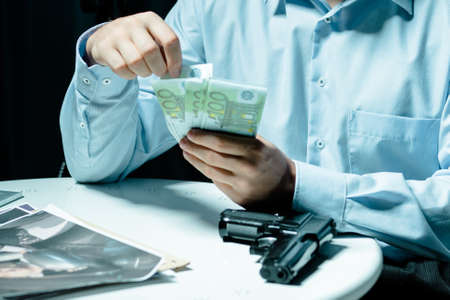 Cropped picture of a man counting money and holding his hands on a table with a gunの写真素材