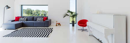 White interior of a living room with a piano, couch with cushions, lamp, red armchair and striped carpetの写真素材