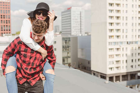 Young hipster couple with the man giving the woman a piggyback on the roof in city centerの写真素材