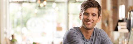 Positive portrait of a young man sitting at the bar of a blurred coffeehouse