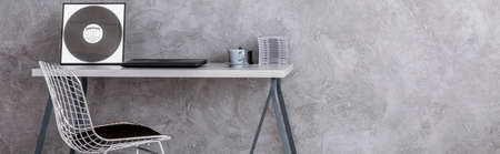 Panoramic picture of a desk and a chair against a grey wall