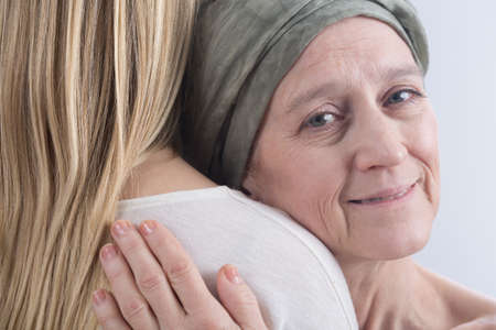 Woman after chemotherapy is hugging to her daughter with a smileの写真素材