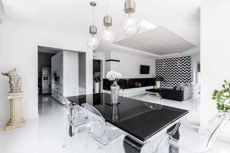 Luxurious black and white dining room with black table and ghost chairs, open living room in the backgroundの写真素材