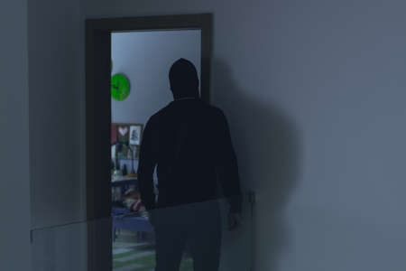 Masked burglar looking into a kid's room through an open doorの写真素材