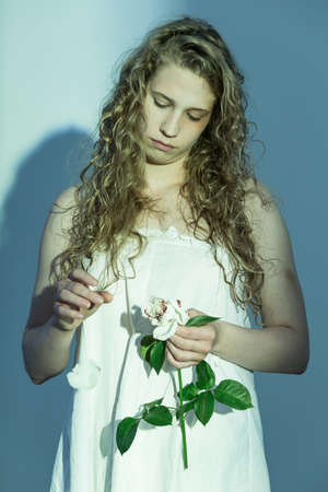 Sad and pensive woman torns white rose petalsの写真素材