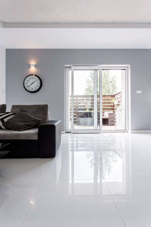 Light villa interior with high gloss flooring, balcony doors and dark sofa