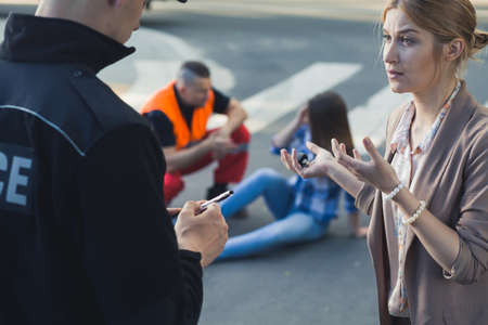 Woman talking with the police officer with the casualty of car accident at the backgroundの写真素材