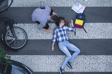 Hurt casualty of a crash lying on the road with the bike and a man giving her the first aidの写真素材
