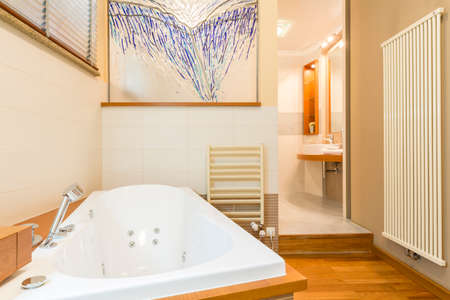 Spacious bathroom with white tiles, floor panels, big bathtub, basin and decorative wall picture