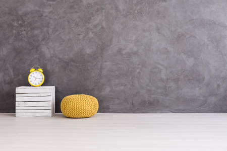 Yellow pouf and clock on a wooden box on a background of a gray concrete wallの写真素材