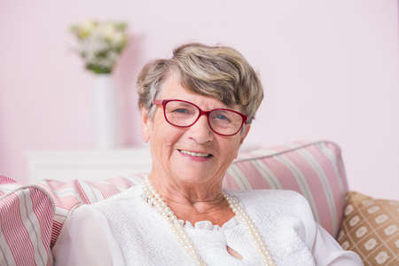 Portrait od smiled senior woman sitting on a couch with pillows