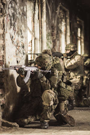 Soldiers in camouflage clothes and helmets kneeling close to the wall with weapon in a scruffy and ruined wallsの写真素材