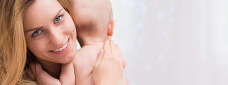 Close-up portrait of a cheerful mother hugging her infant babyの写真素材