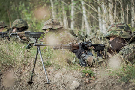 Soldiers laying on a training ground with the weapon with the forest behind them