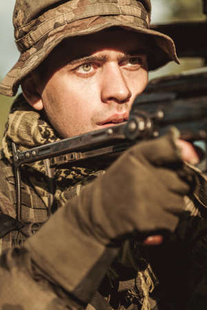 Close shot of a concentrated soldier in camo hat, pointing a gun