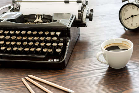 Closeup shot of a desk with a vintage typewriter, cup of coffee, pencils and a clock