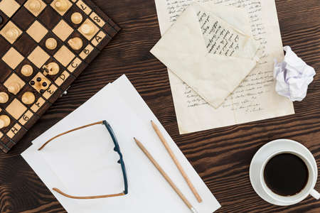 Top view of a brown desk with a sheets of paper, glasses, old letters and pencilsの写真素材