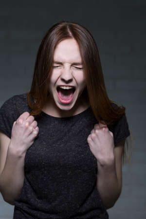 Portrait of long haired girl, who is shouting and clenching her fistsの写真素材