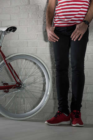 Shot of man's legs standing close to the modern bibycle's back wheel at the white brick wall backgroundの写真素材
