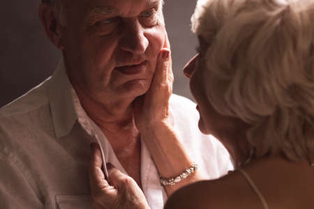 Elder couple standing close each other, with the woman's hands touching man's face and shirtの写真素材