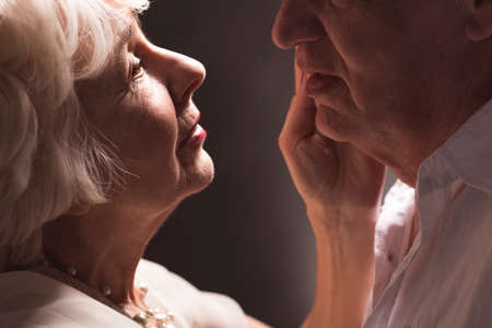 Elder couple faces close to each other with woman's hand touching man's faceの写真素材